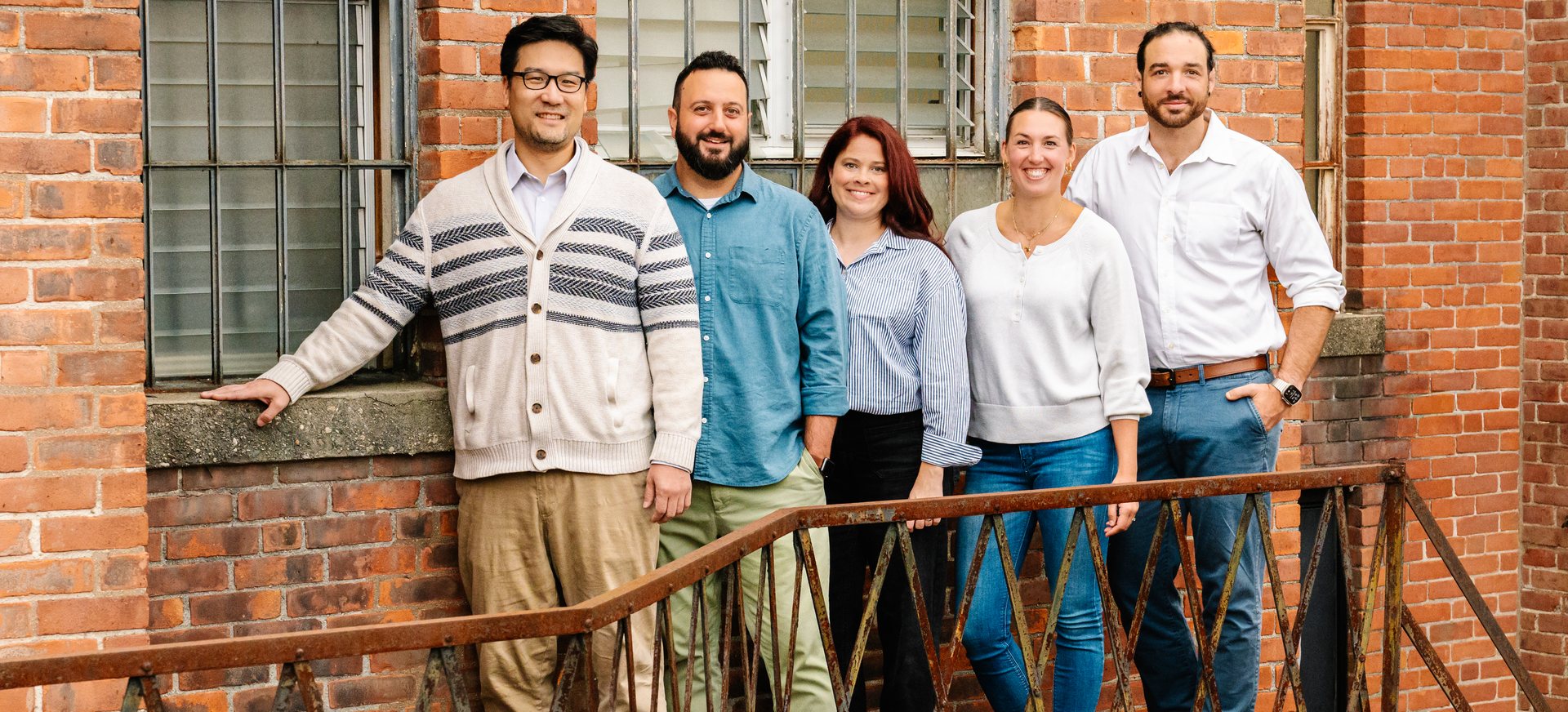The five clinician-owners of Waypoint Cooperative standing together on the iron fire escape of a brick mill building in Torrington